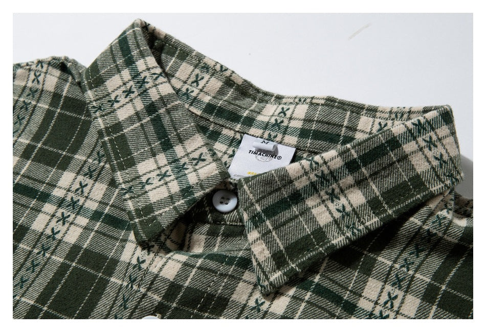 Close-up of the pointed collar and top button on a dark green and cream plaid shirt.