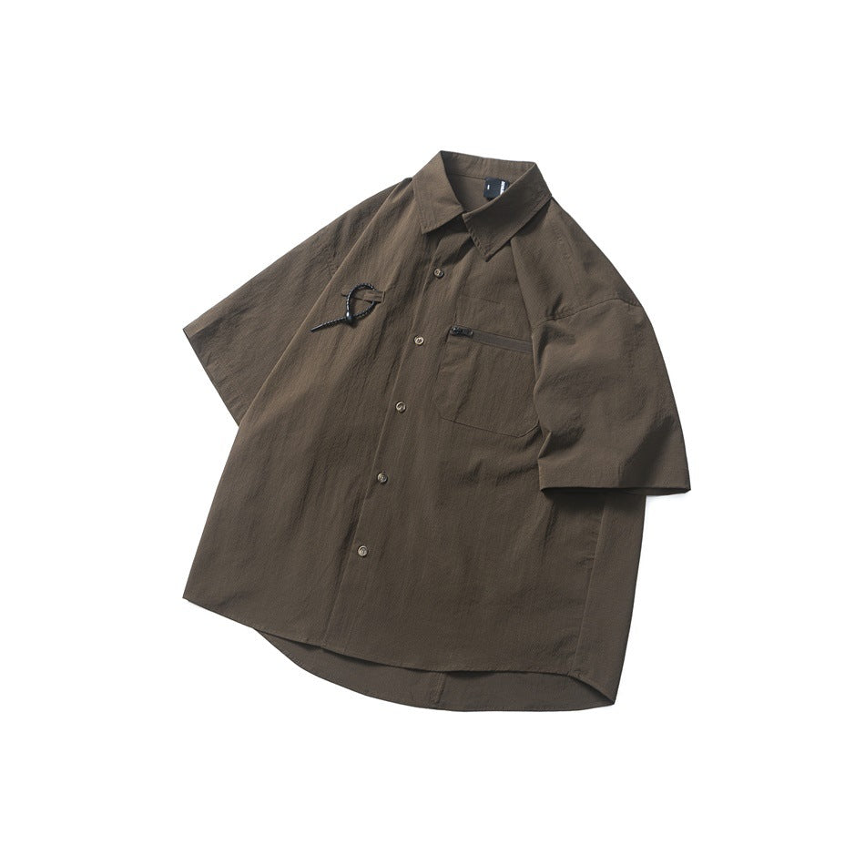 Flat lay of a dark brown short-sleeve button-up shirt with a pointed collar, chest pocket, and black chest detail.