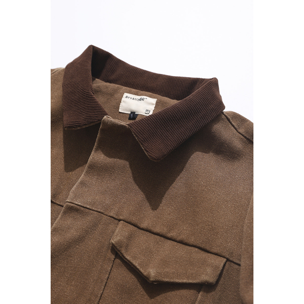 Close-up of a brown jacket's dark ribbed collar and flap chest pocket.