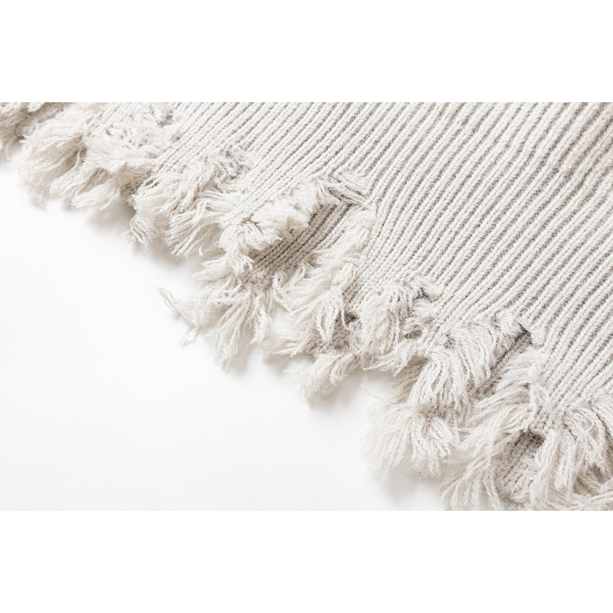 Close-up of an ivory rib-knit sweater hem with loose, distressed fringe.