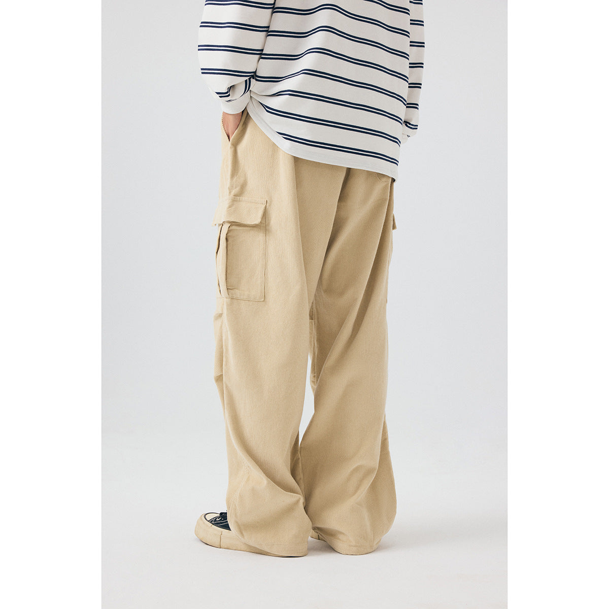 Model wearing loose beige cargo pants with a flap thigh pocket, shown from the side with the upper body cropped.