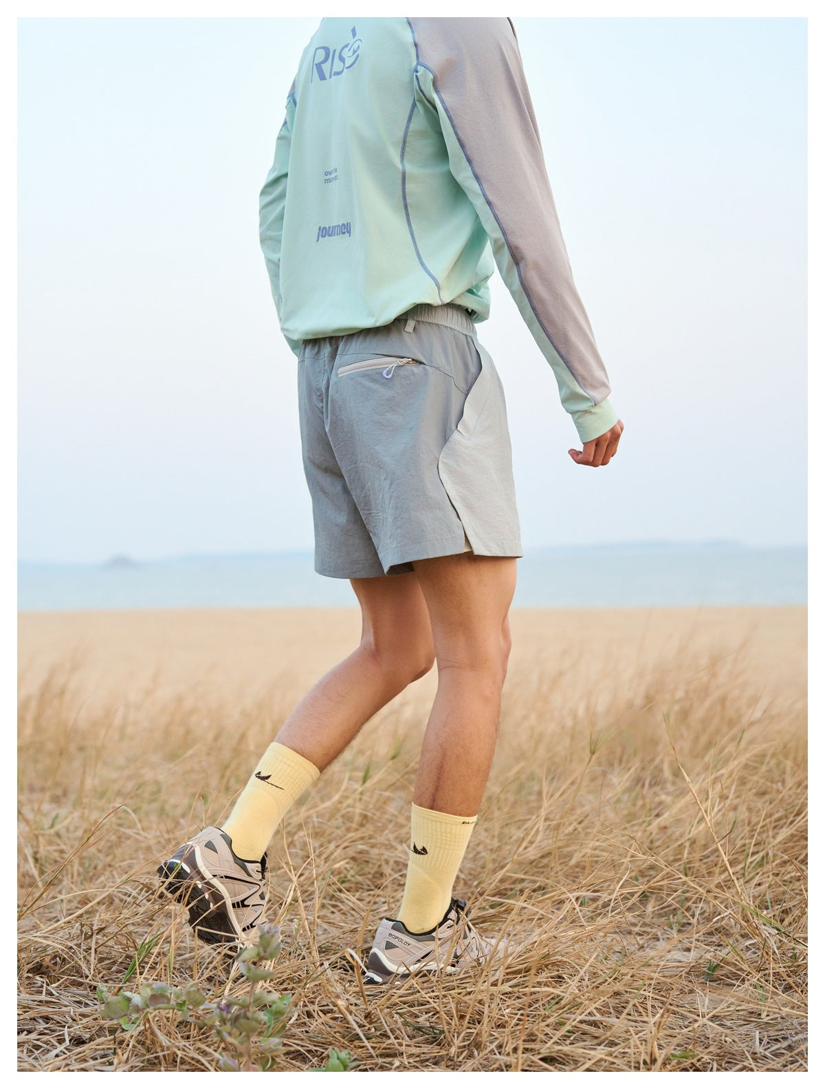 Side and back view of gray shorts with a zip pocket, worn with a mint-and-gray printed shirt.