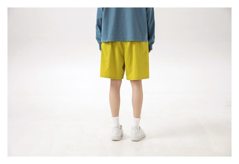 Back view of a model wearing bright yellow shorts with a blue long-sleeve shirt and white sneakers.
