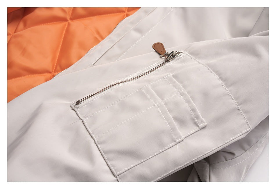 Close-up of a light gray jacket sleeve with a zippered pocket and orange quilted lining visible behind it.