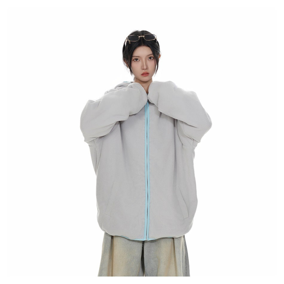 Model wearing a zipped light gray hooded jacket with pale blue trim and loose light-wash jeans.