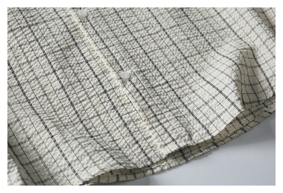 Close-up of an off-white shirt with a black windowpane check, front buttons and curved hem.