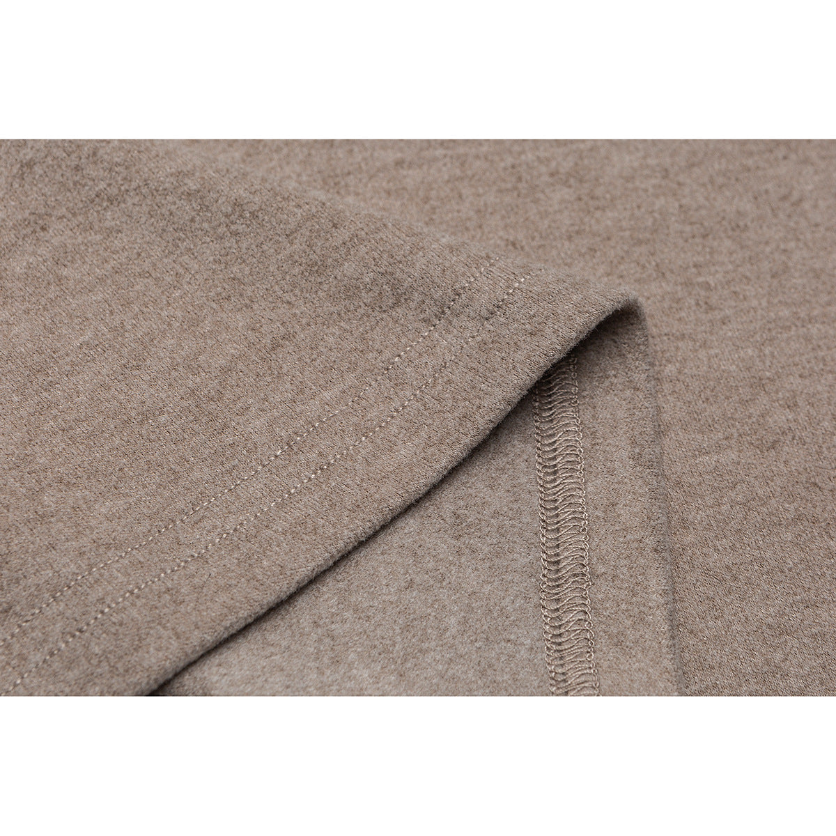 Close-up of a taupe shirt hem showing the folded edge and overlock stitching.