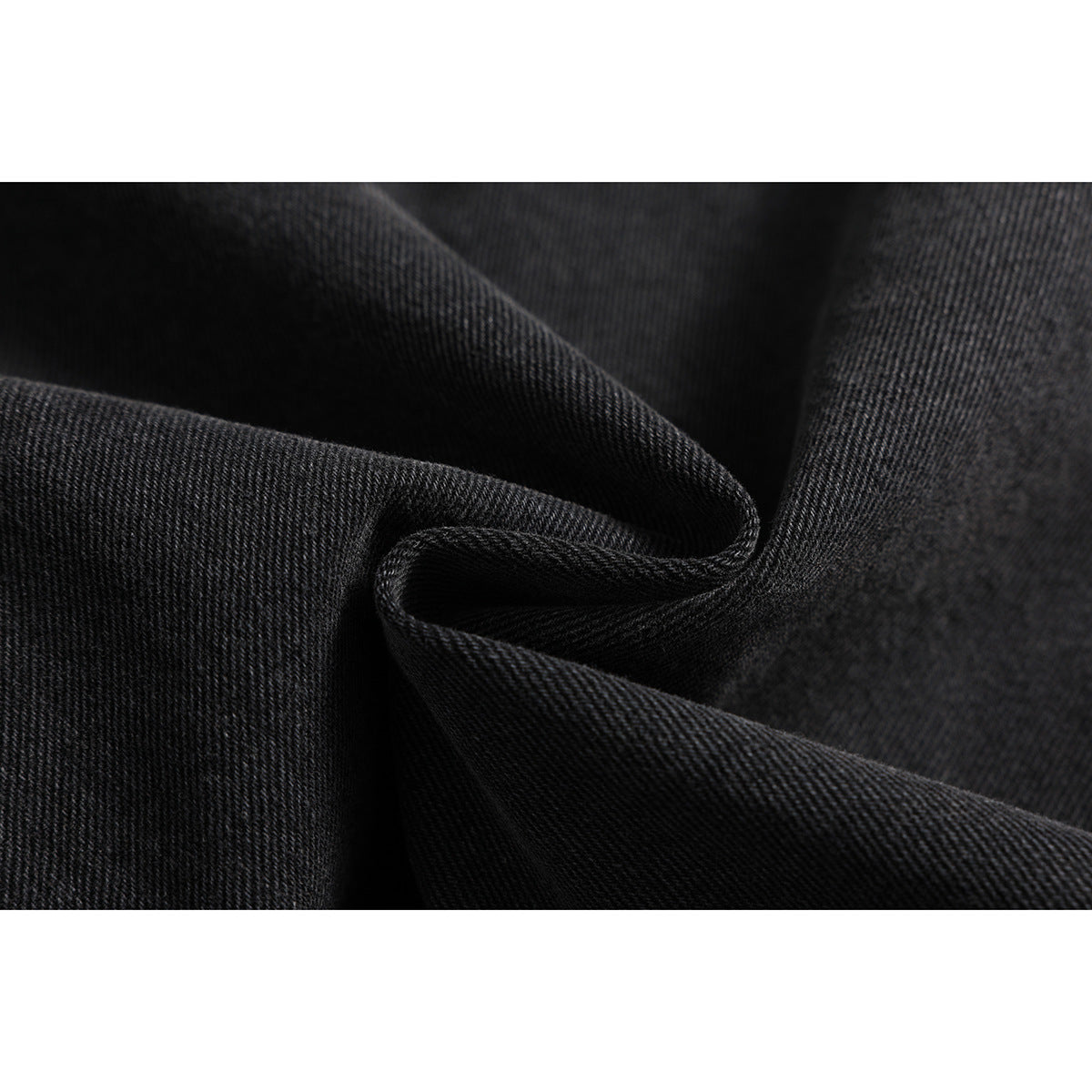 Macro view of folded charcoal-black denim fabric showing its diagonal weave and texture.