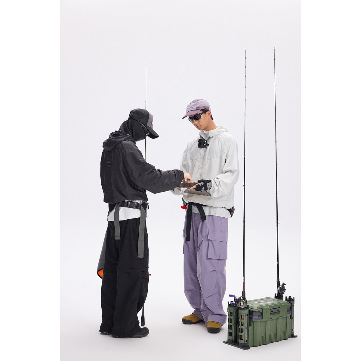 Two models in outdoor fishing outfits stand beside fishing rods and a green tackle case.
