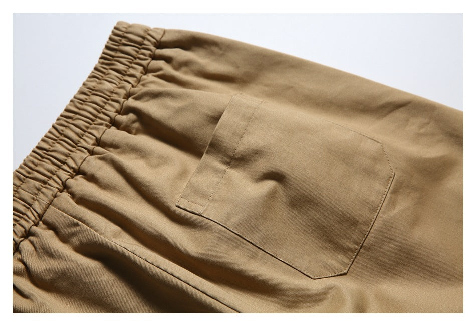 Close-up of tan bottoms showing a gathered elastic waistband and a stitched rectangular patch pocket.