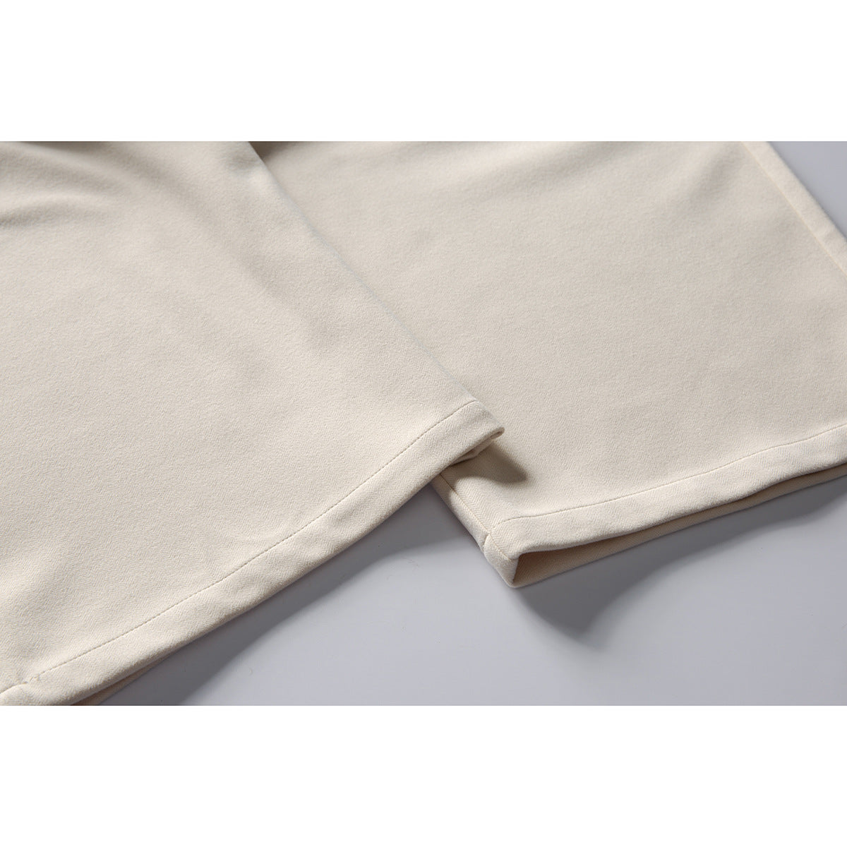 Close-up of the neatly stitched hems of cream-colored trousers.