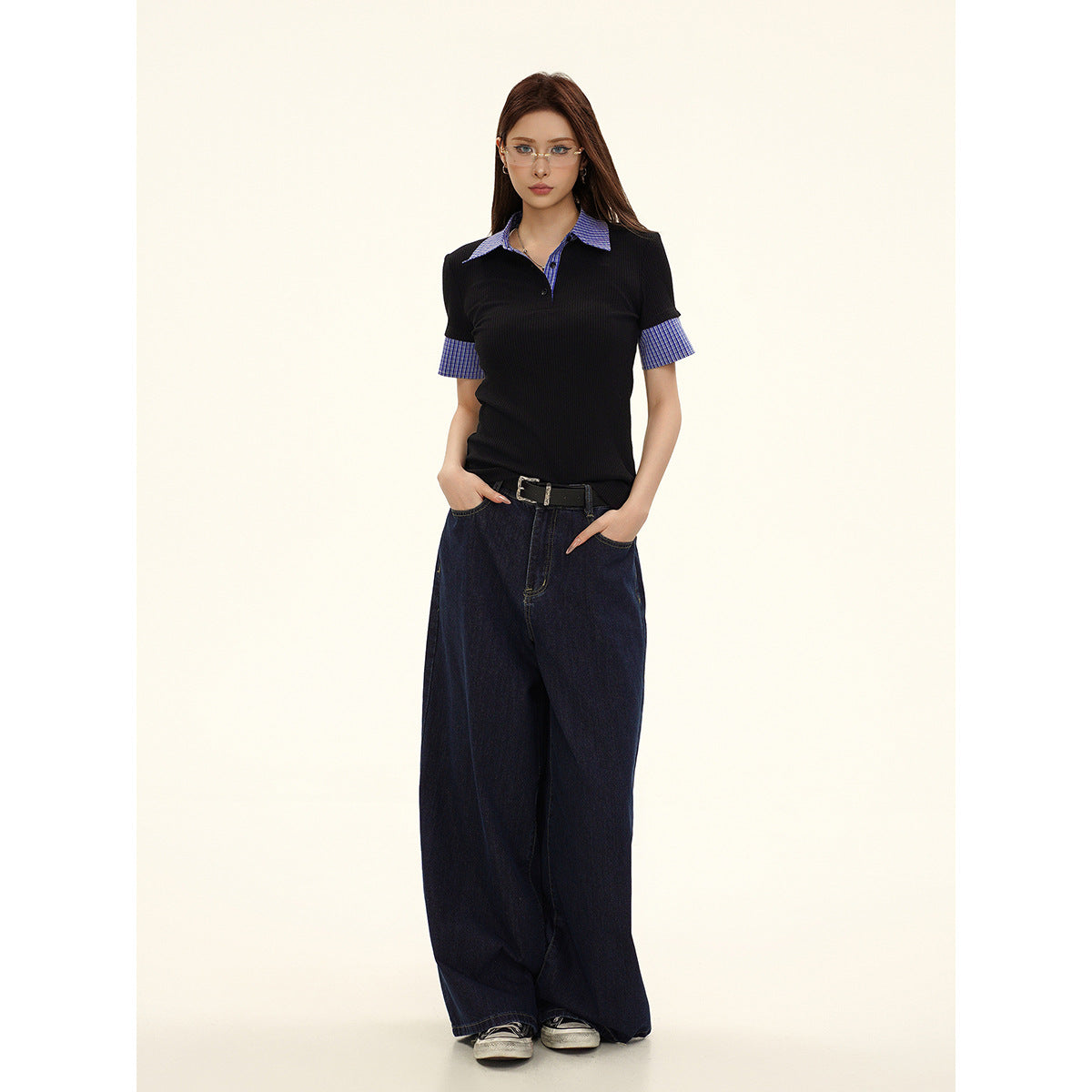 Full-length front view of a model wearing a black polo with blue check accents and dark wide-leg jeans.