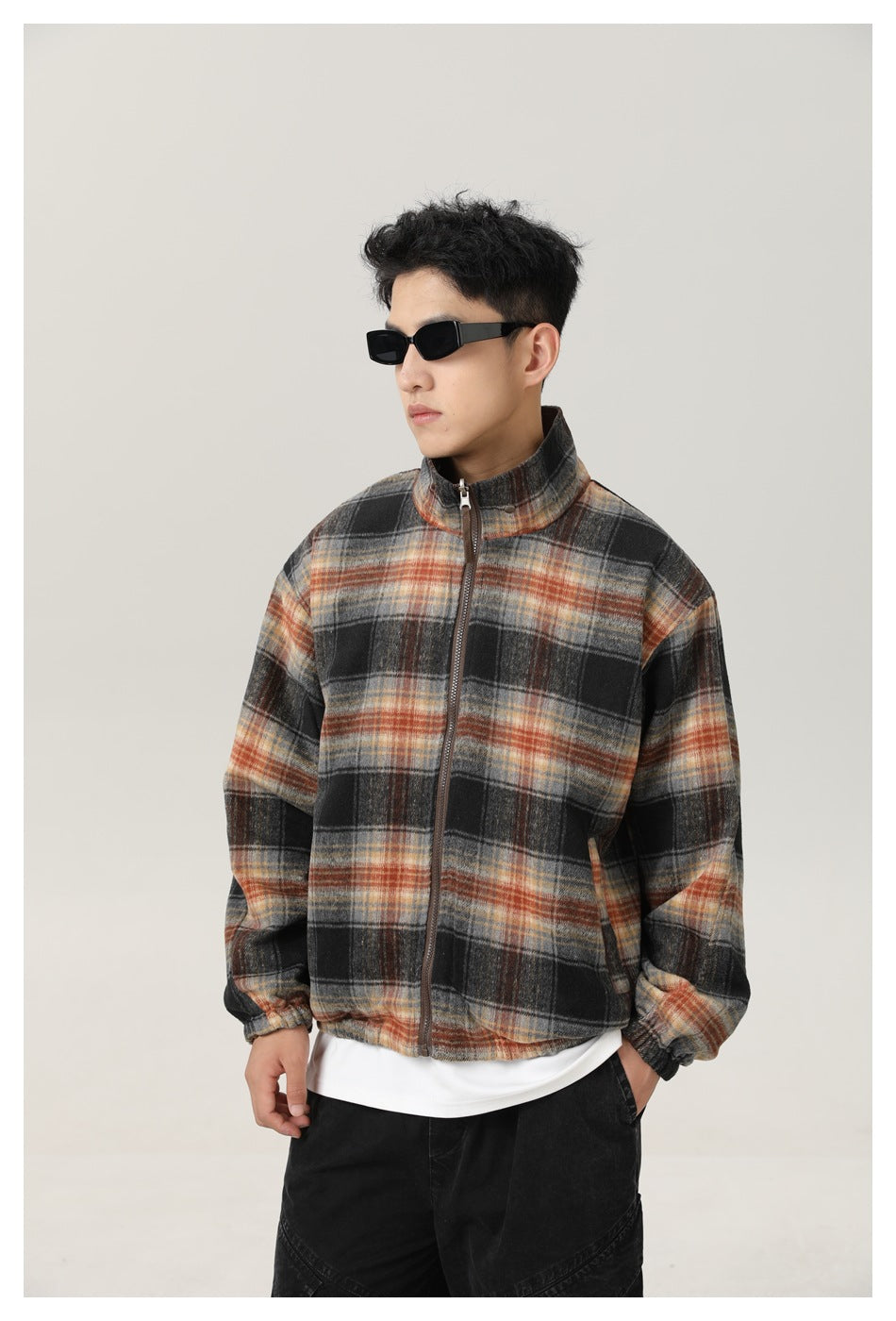 Closer view of a man wearing a black, gray, and rust plaid jacket, showing its zip front and stand collar.