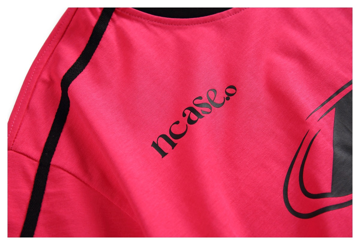 Close-up of the bright pink T-shirt’s front, showing black shoulder piping and printed graphics.
