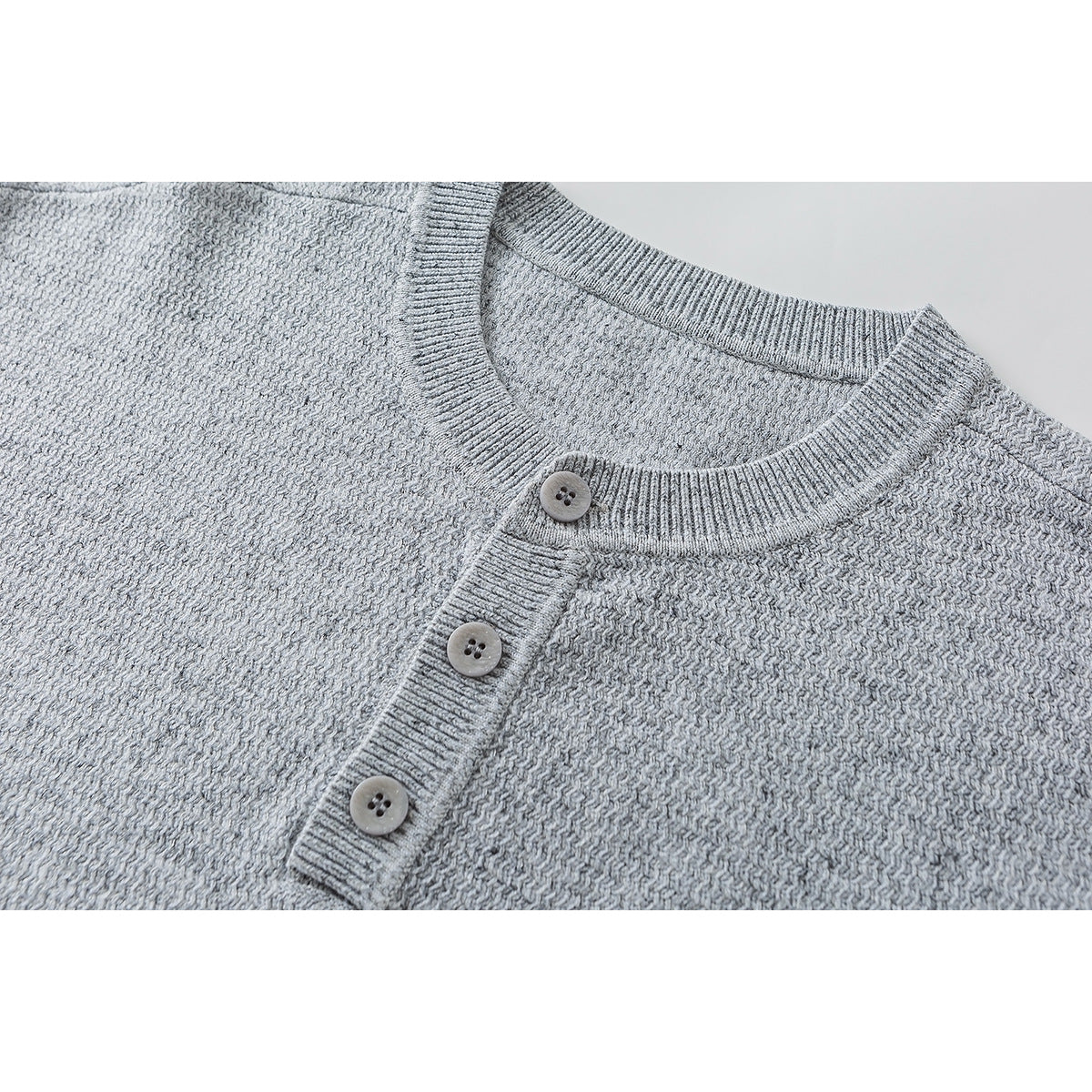 Close-up of a light gray knit sweater's ribbed crew neck and three-button placket.