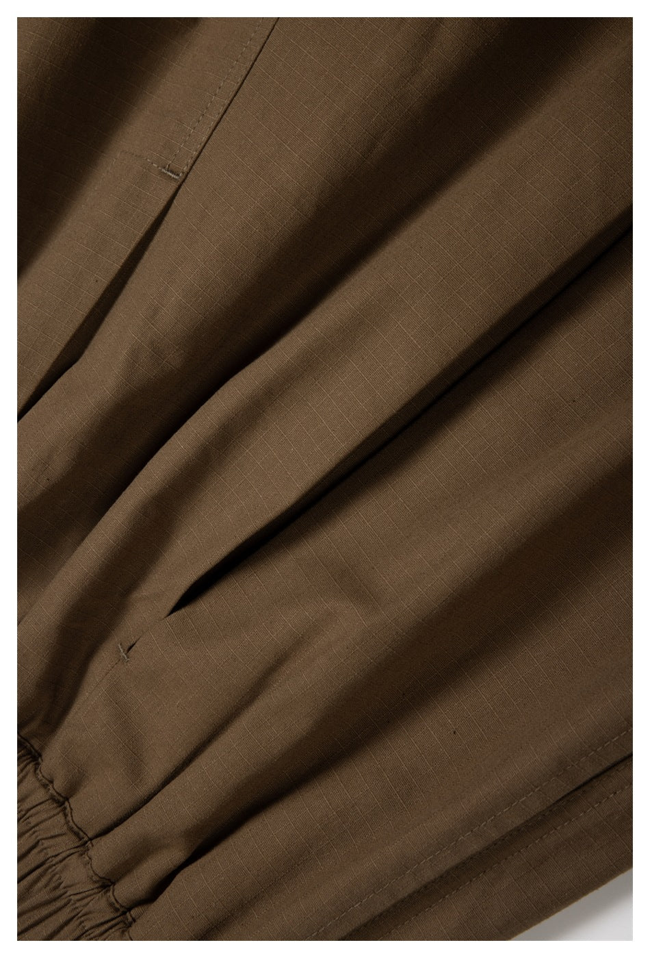 Close-up of brown trouser fabric, folds, stitching, and an elasticized edge.