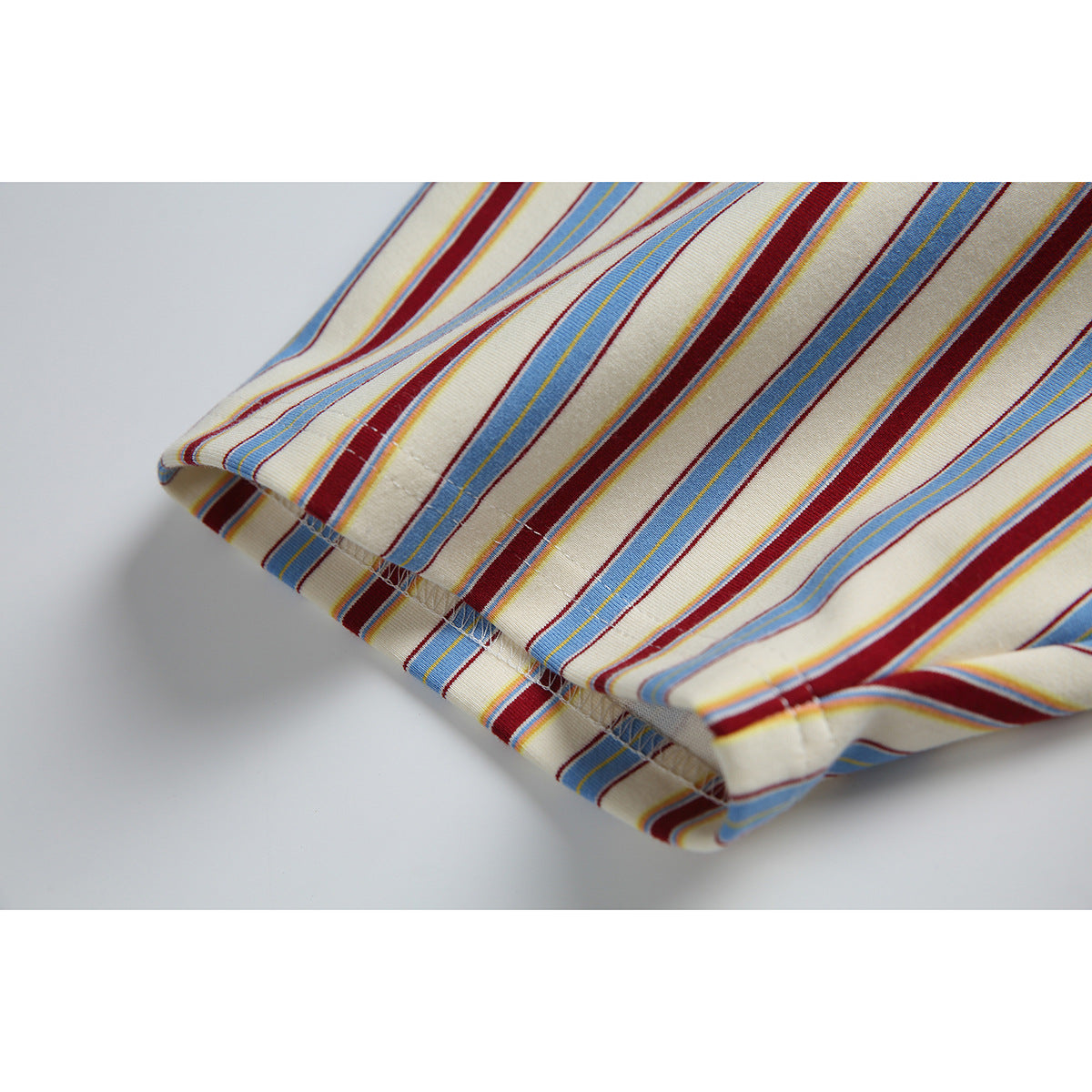Close-up of the striped T-shirt's folded hem and stitching in cream, blue, and burgundy.