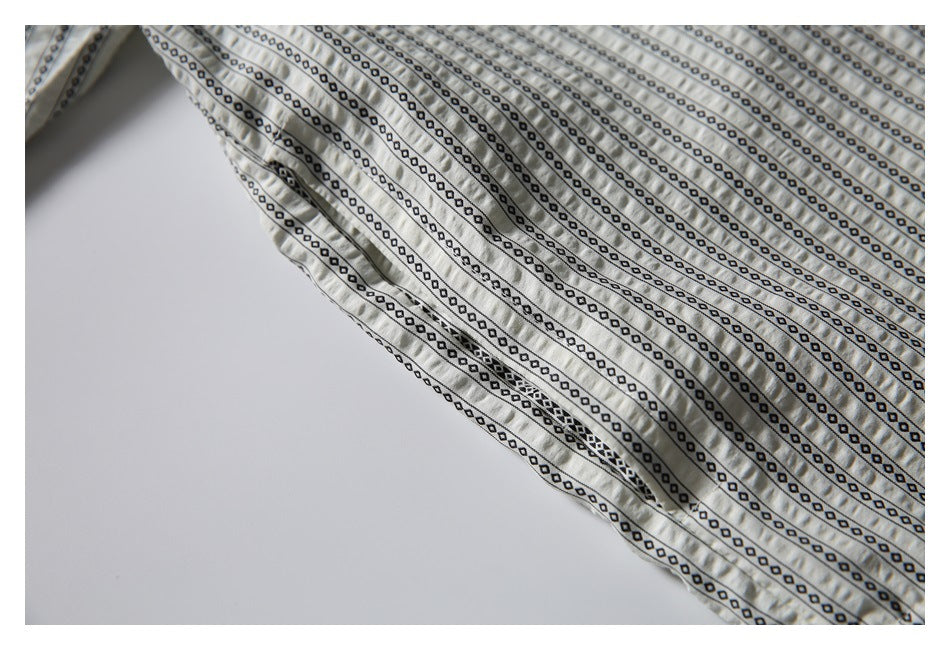 Close-up of a cream shirt with narrow black geometric stripes and a stitched seam.