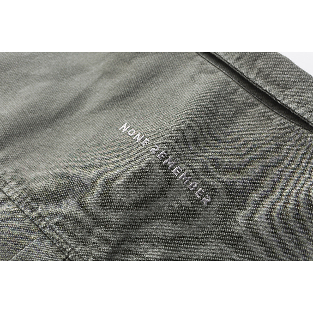 Close-up of small white embroidered lettering on charcoal gray shirt fabric.