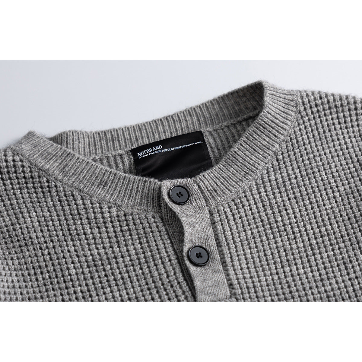 Close-up of a gray waffle-knit sweater neckline with ribbed trim, two dark buttons, and a black neck label.