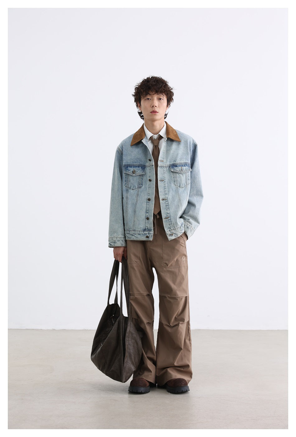 Model wearing light blue washed denim jacket with brown collar over a white shirt, brown tie and wide brown pants
