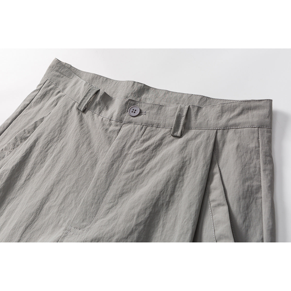 Close-up of gray shorts showing the waistband, button, belt loops, stitching, and front pocket seam.