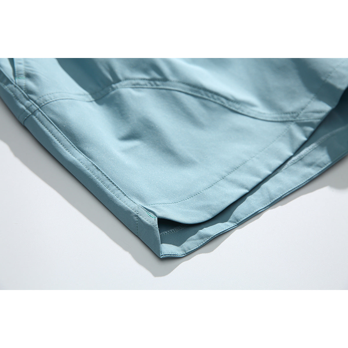 Close-up of the hem and curved seam on light blue shorts.