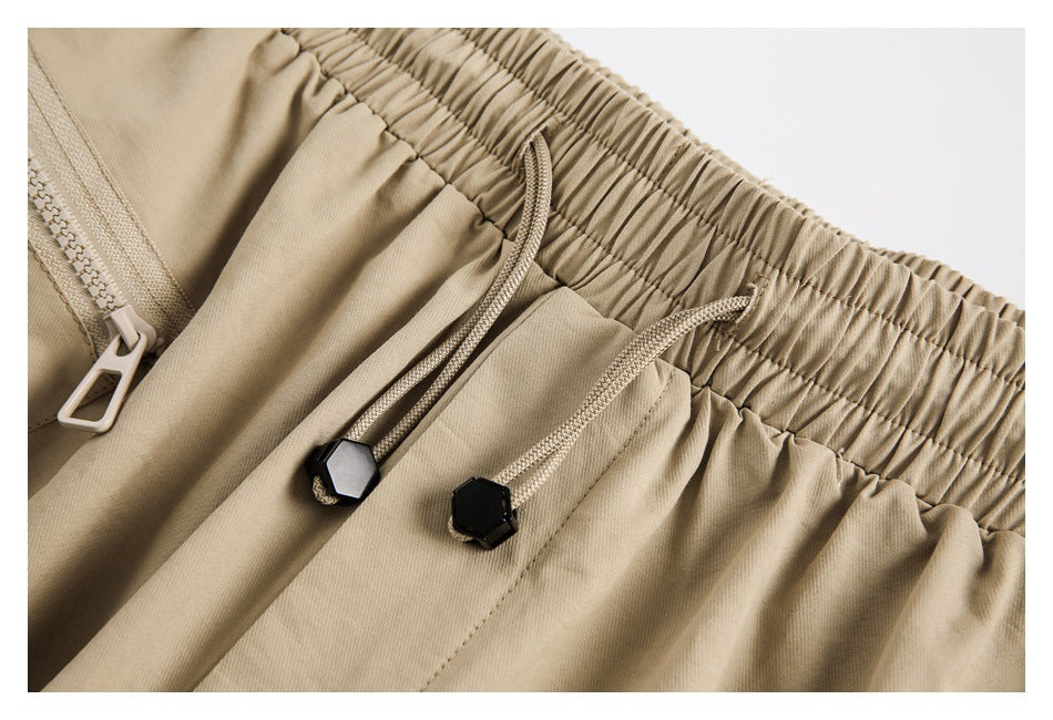 Close-up of beige pants showing the gathered elastic waist, drawcords with black toggles, and zipper.