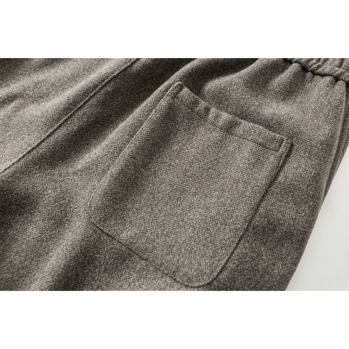 Close-up of a large patch pocket on taupe pants, with the elastic waistband partly visible.