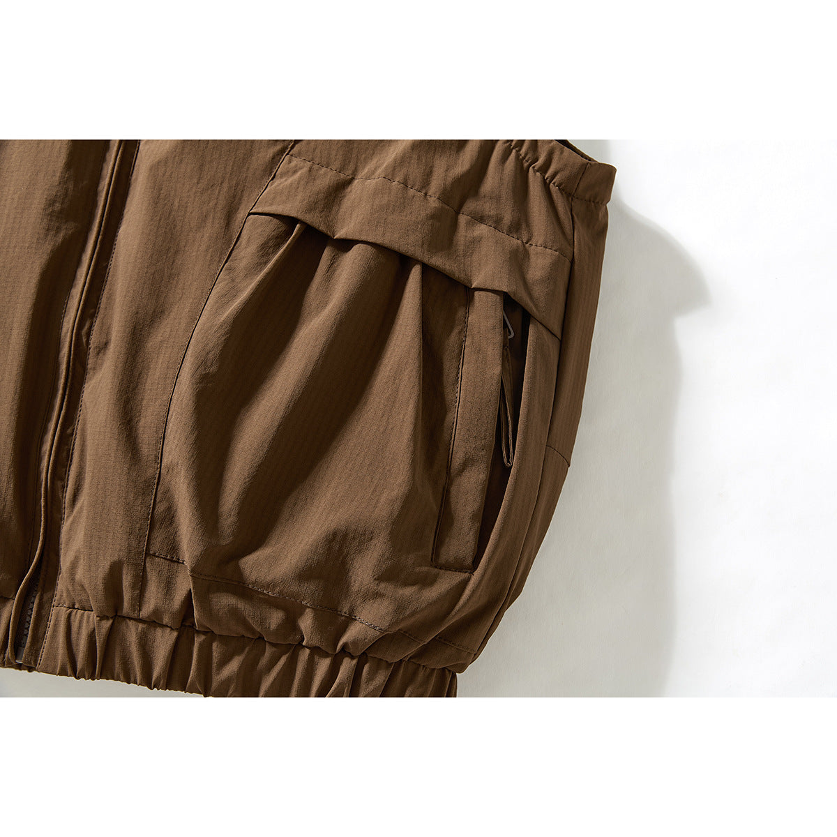 Close-up of a brown vest's gathered lower hem and large side pocket with an overlapping flap.