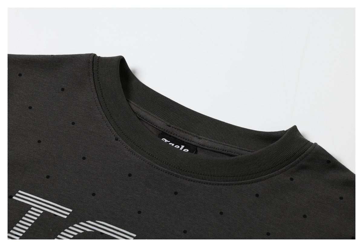Close-up of a charcoal T-shirt neckline with a ribbed collar, scattered black dots and partial white lettering.