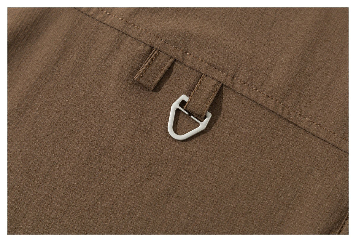 Close-up of a small silver metal loop attached to a fabric tab along a seam of the brown shirt.