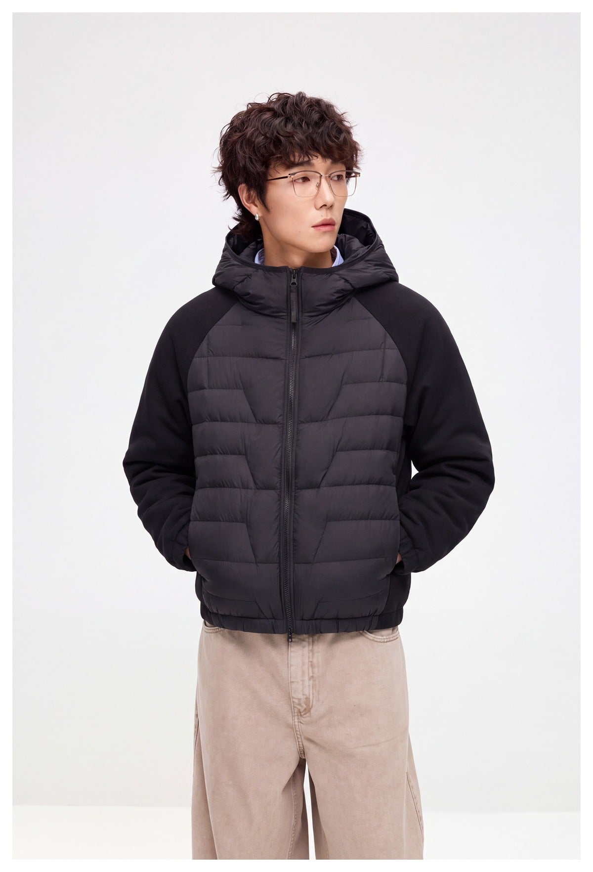 Front view of a model wearing a black hooded jacket with horizontal quilted panels, solid sleeves, and a full-length zipper.