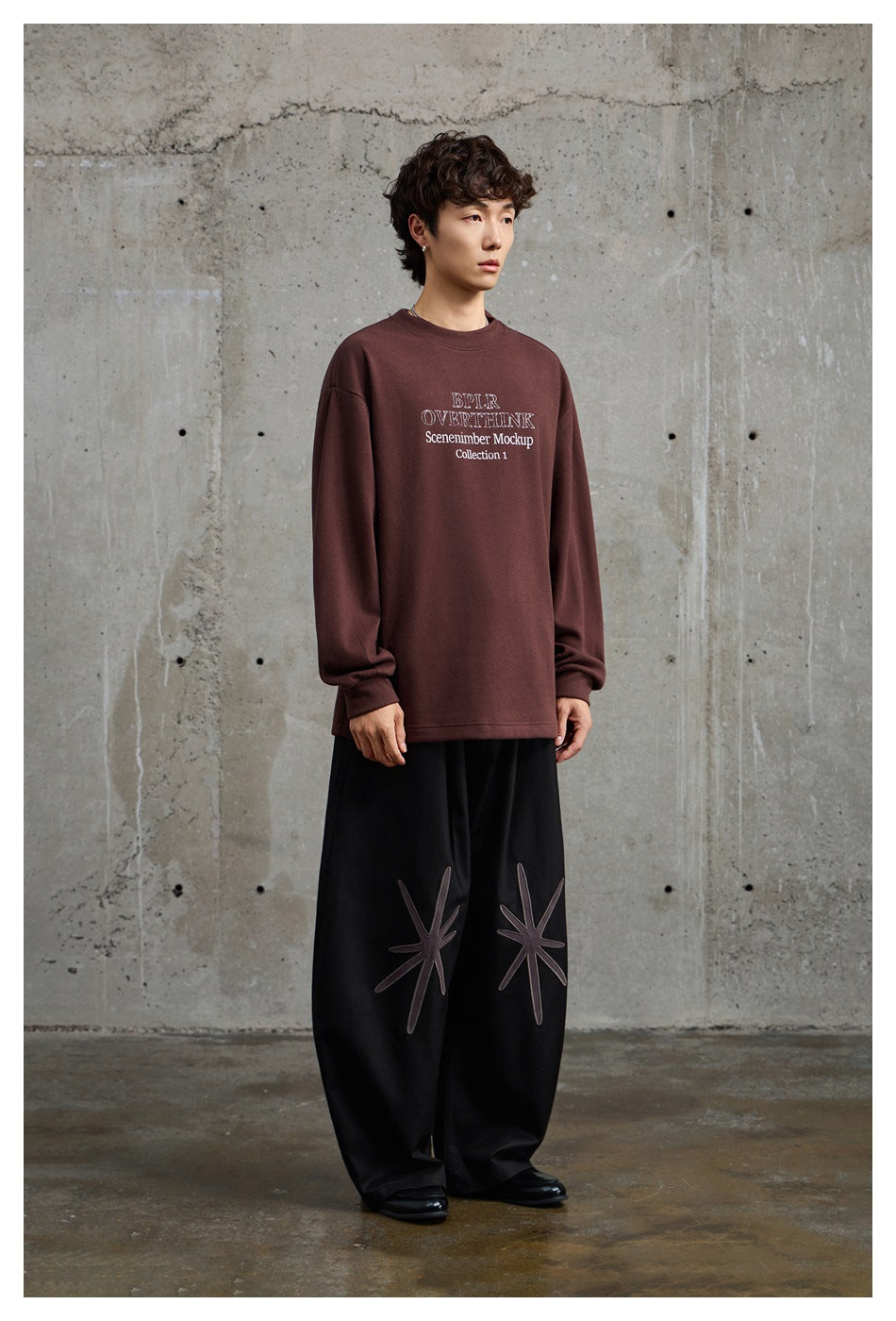 Three-quarter view of a model wearing a burgundy oversized printed sweatshirt and black wide-leg trousers with starburst
