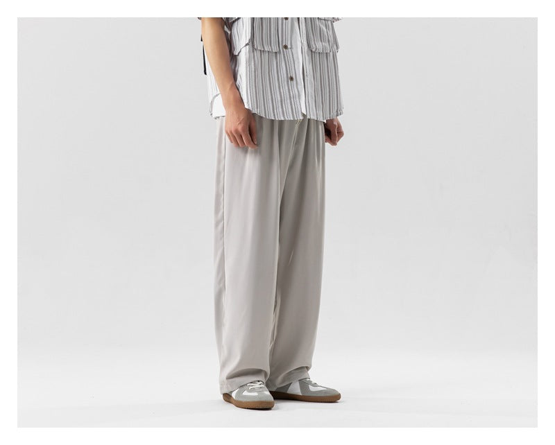 Side-front view of a person wearing light beige wide-leg pleated pants with a striped shirt and sneakers