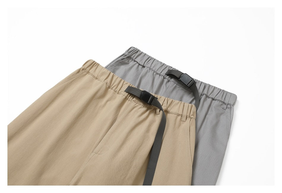 Cropped view of tan and gray pants side by side, highlighting elastic waistbands and black buckle straps.