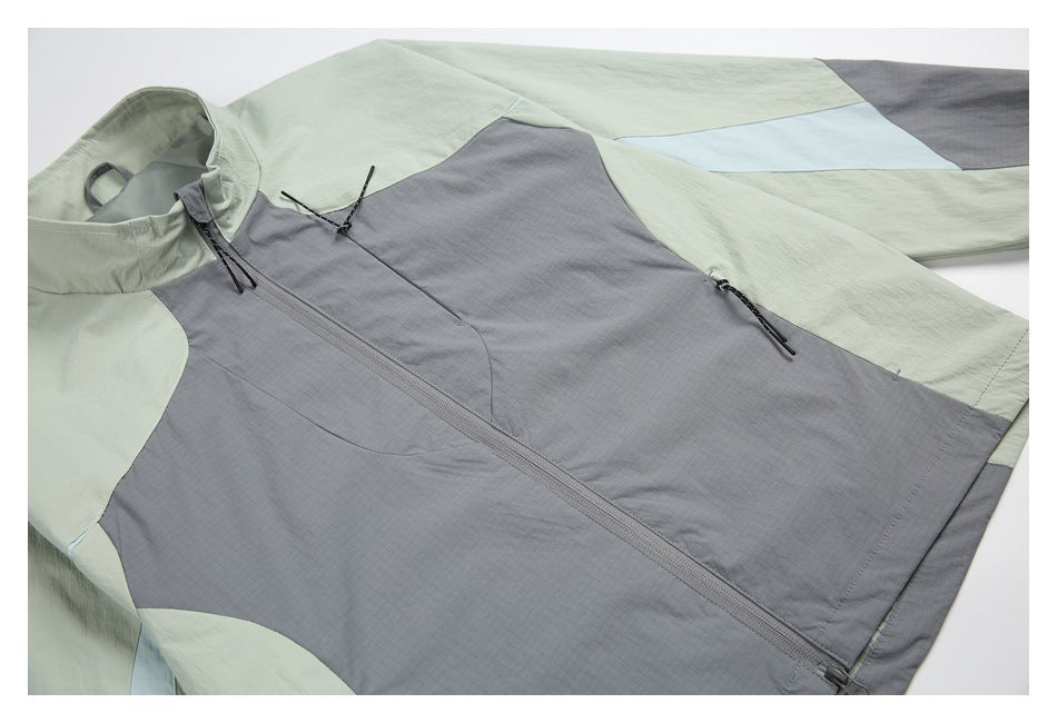Close view of a gray and pale sage color-block jacket laid flat, showing the front zipper and zip pockets.