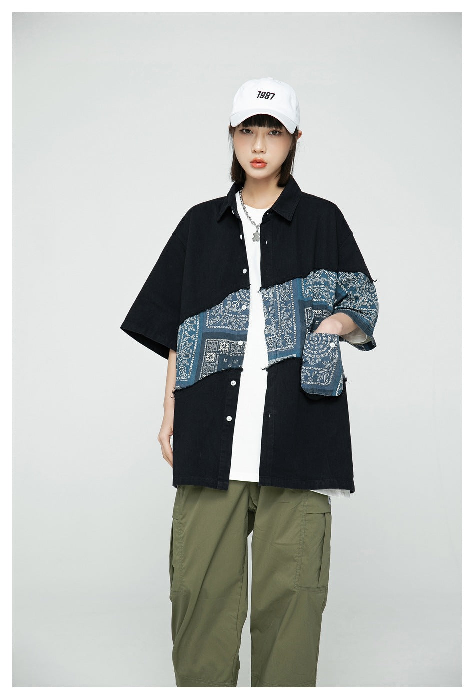 Front view of a model wearing an oversized black button-up shirt with a blue bandana-print panel and olive cargo pants.