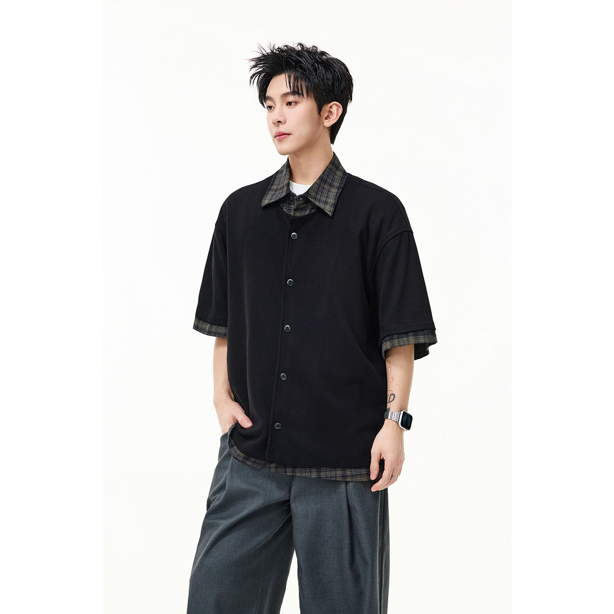 Model wearing a black short-sleeve button-front overshirt with dark plaid collar, cuffs and hem, paired with wide gray