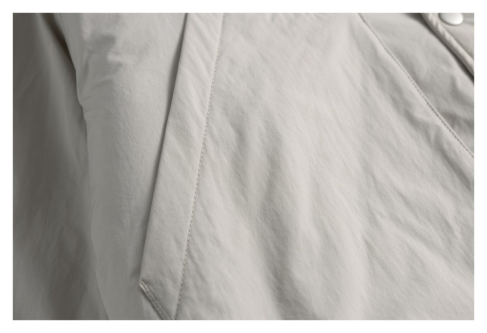 Close-up of pale gray garment fabric with a stitched diagonal panel seam and a partial button.