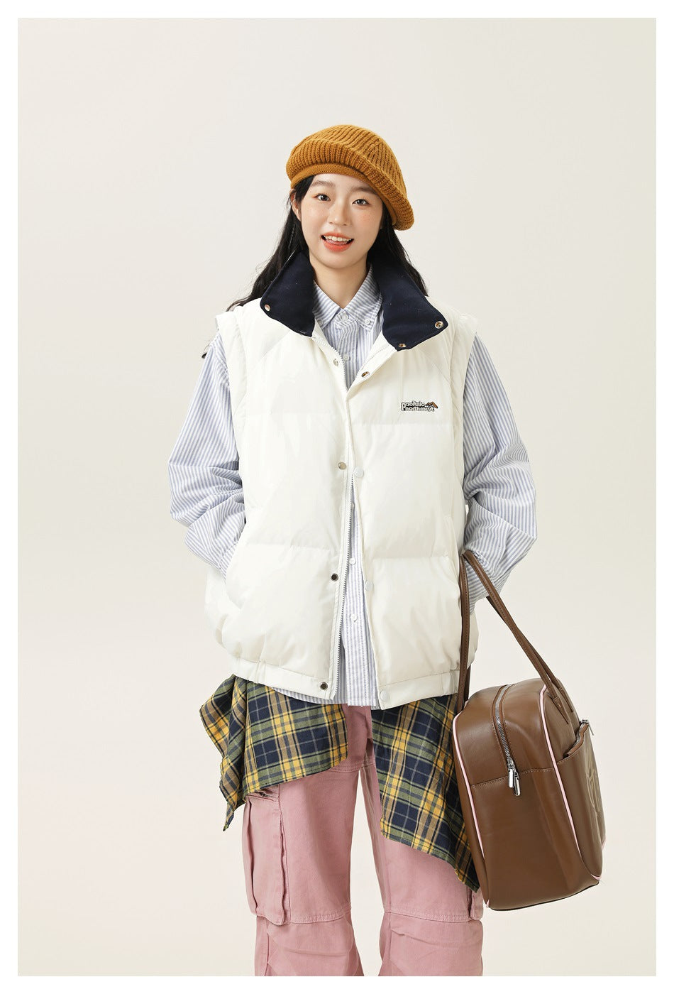 A closer view of a model wearing a white padded vest with a navy collar over a striped shirt.