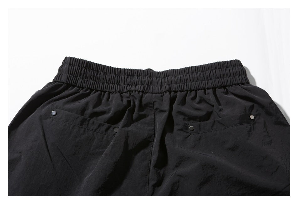 Back view of black shorts laid flat, showing the elastic waistband and two snap-trimmed pockets.