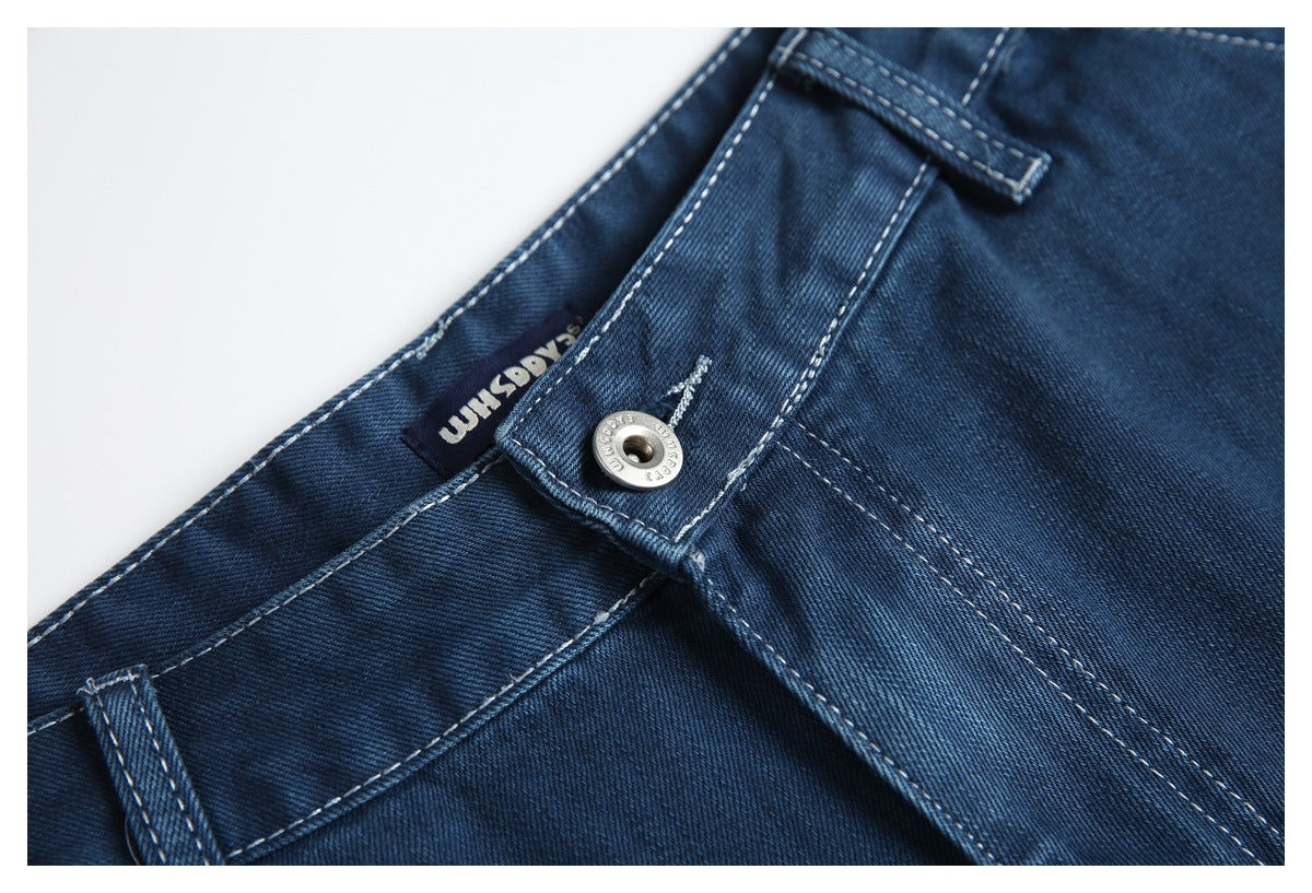 Close-up of dark blue jeans showing the waistband, belt loop, metal button and inner label.