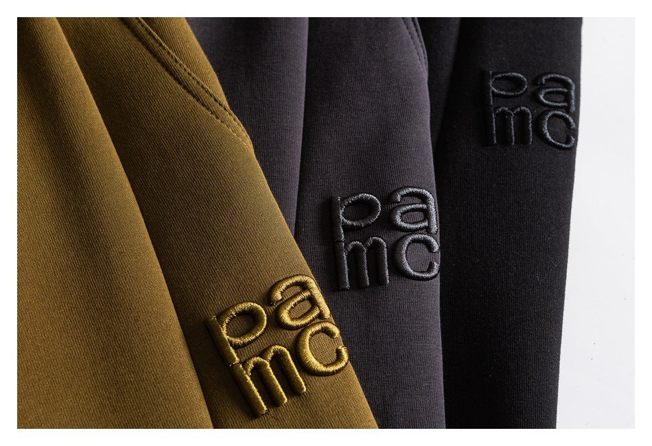 Close-up of embroidered PAC lettering on ochre, charcoal, and black garment fabric.