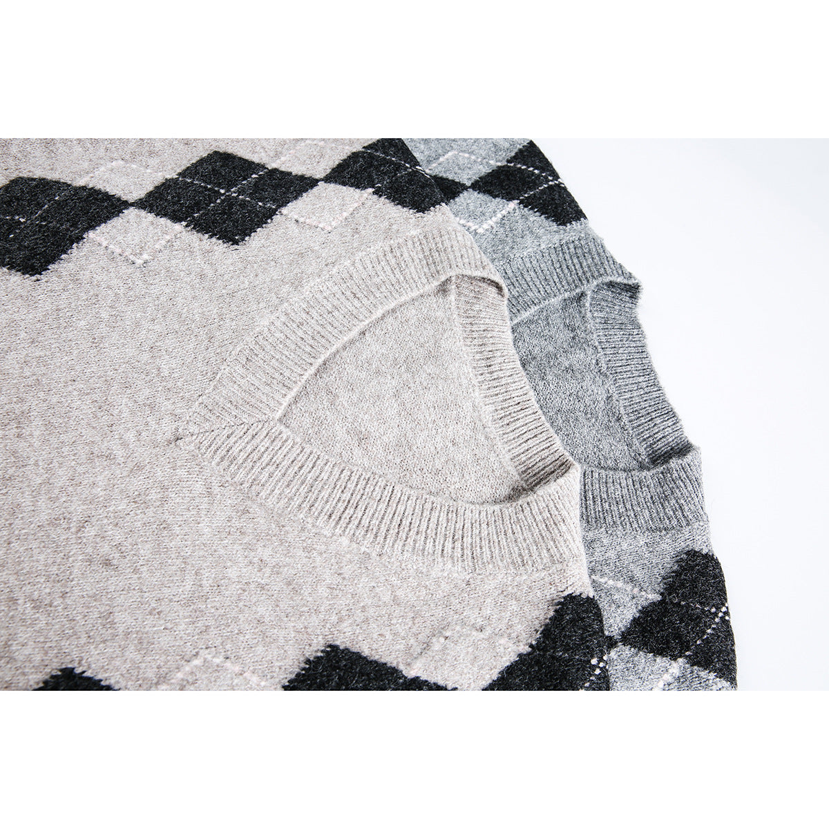 Close-up of overlapping beige and gray V-neck sweaters, showing ribbed necklines and black argyle diamonds.