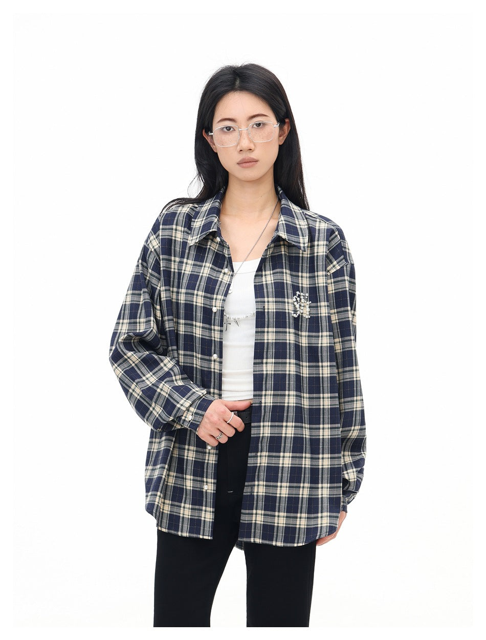 Model wearing an open navy and cream plaid shirt over a white top, with a beaded chest embellishment.
