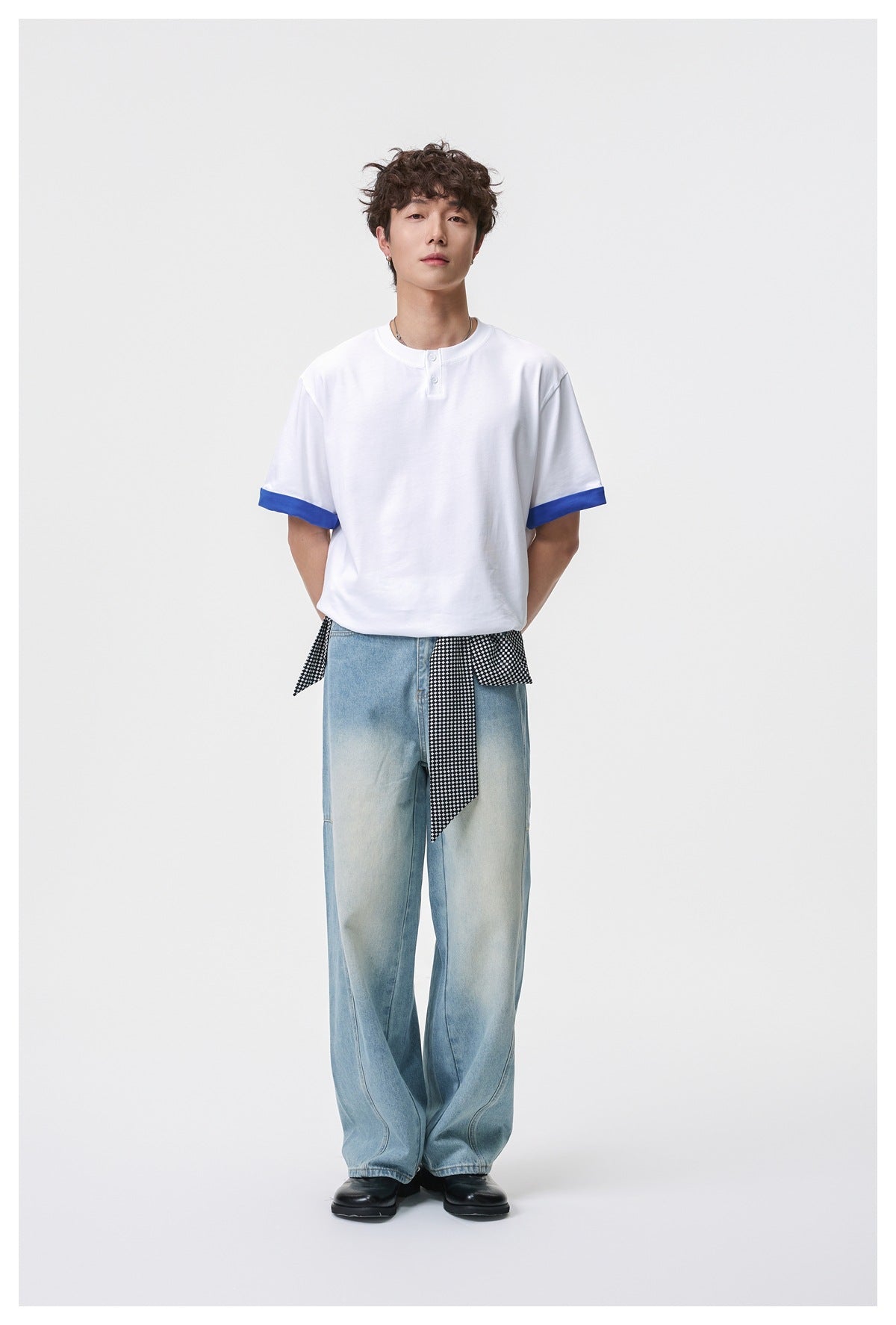 Full-length front view of a model wearing a white henley T-shirt with blue turned-up sleeve cuffs and loose light-wash jeans.