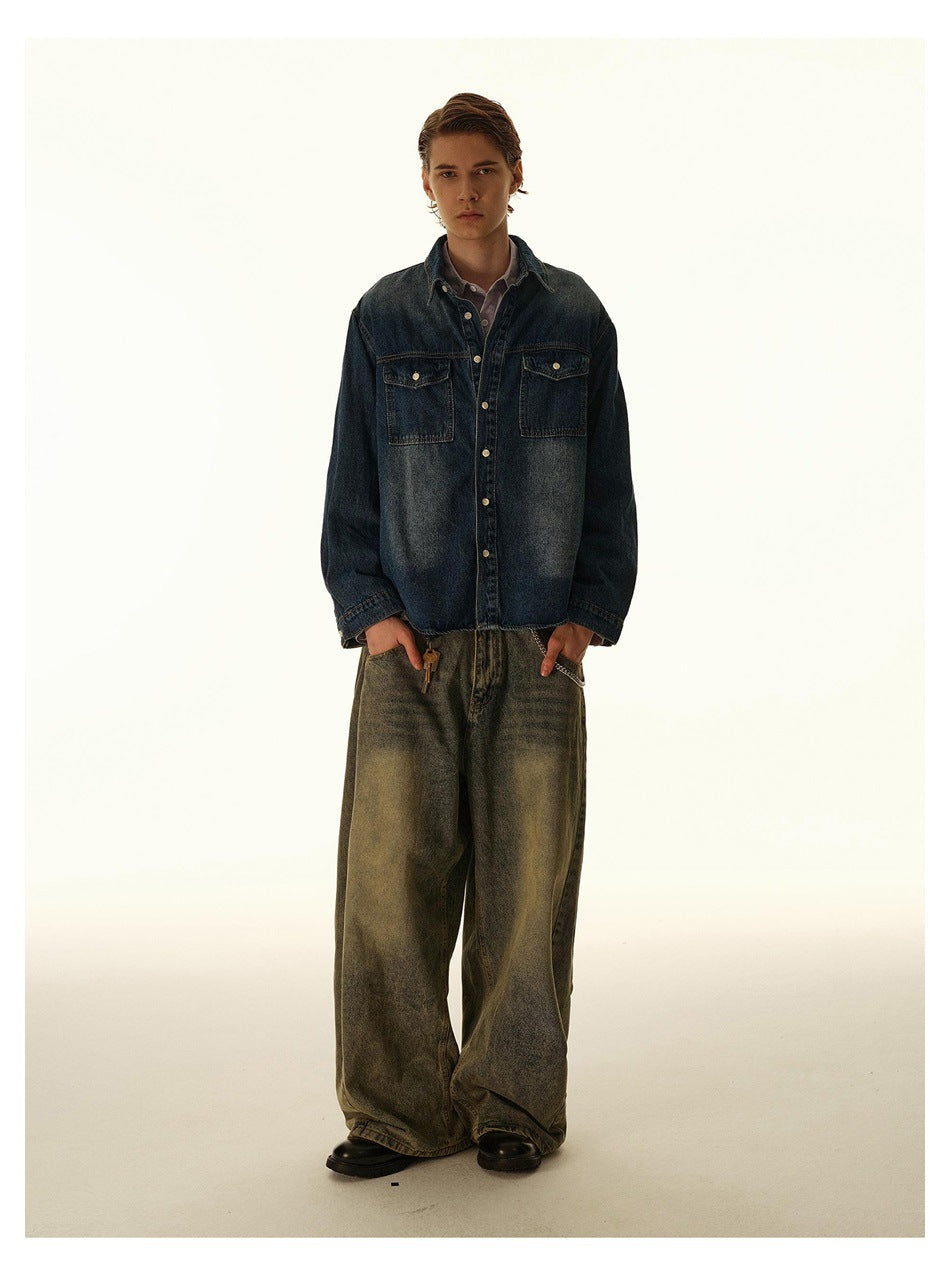 Full-length front view of a model in a dark indigo denim shirt and very wide, faded olive-gray jeans.