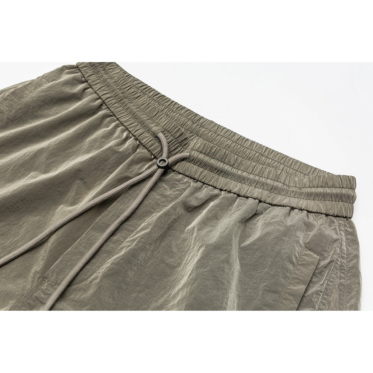 Close-up of olive-gray shorts with a gathered elastic waistband, long drawcords and a side pocket.