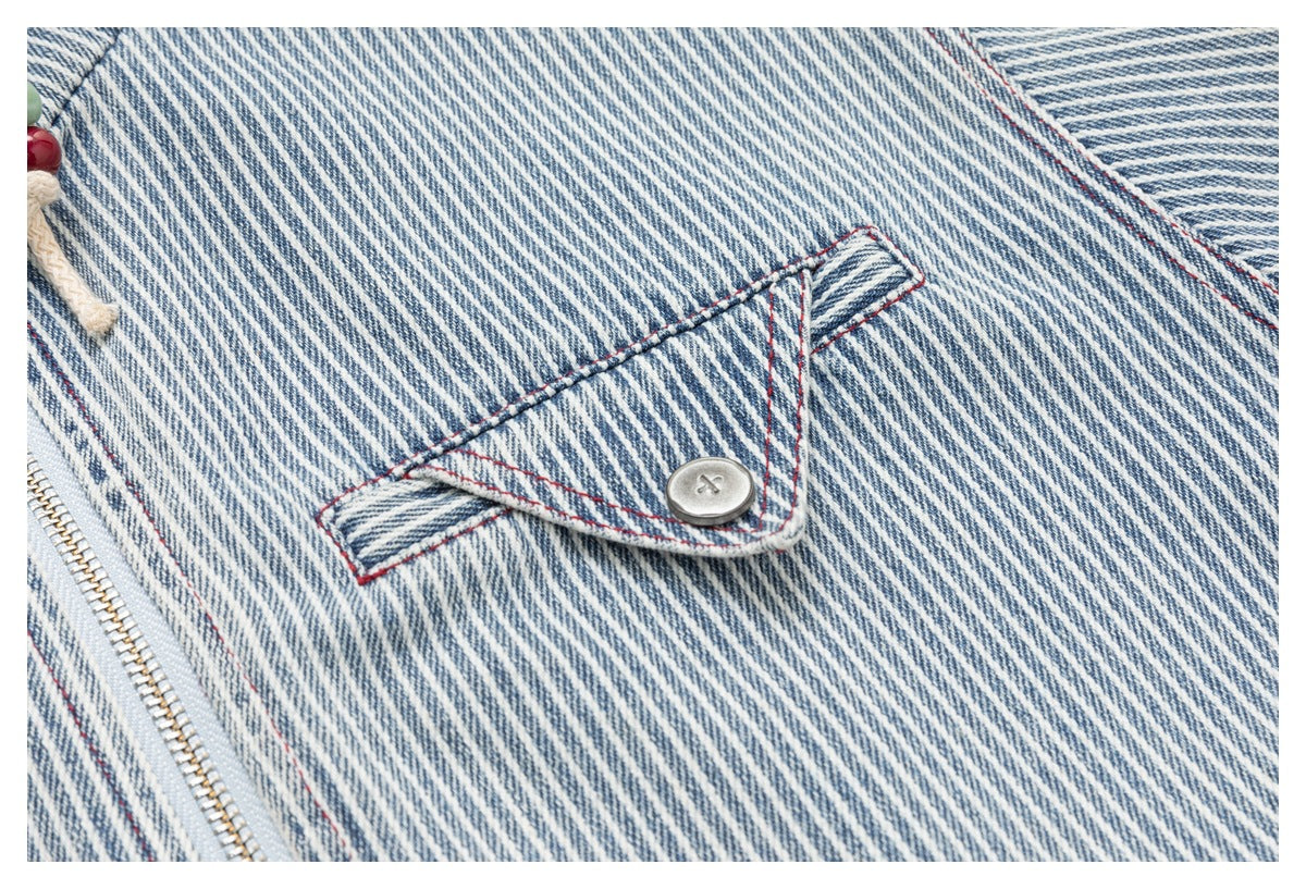 Close-up of a striped garment’s flap pocket with a metal button, red stitching and a zipper.